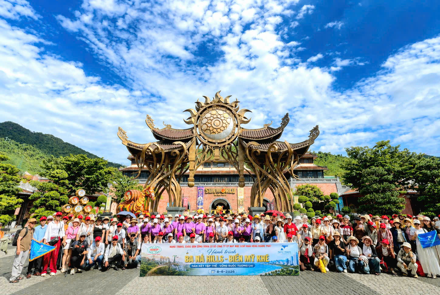 Nhóm du khách chụp ảnh kỷ niệm trước cổng vào Bà Nà Hills, với khung cảnh thiên nhiên tươi đẹp và bầu trời trong xanh.